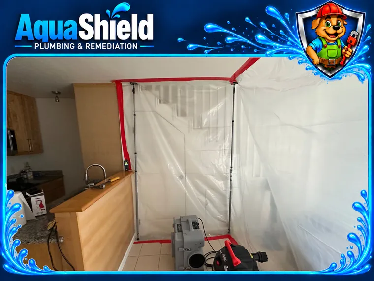The kitchen sealed off with plastic sheeting and red zipper tape, an air scrubber and a vacuum set up inside