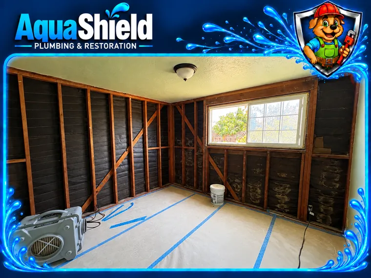 A bedroom with its exterior walls opened to the studs and no insulation in the cavities, floor covered with protection paper, an air scrubber in the corner